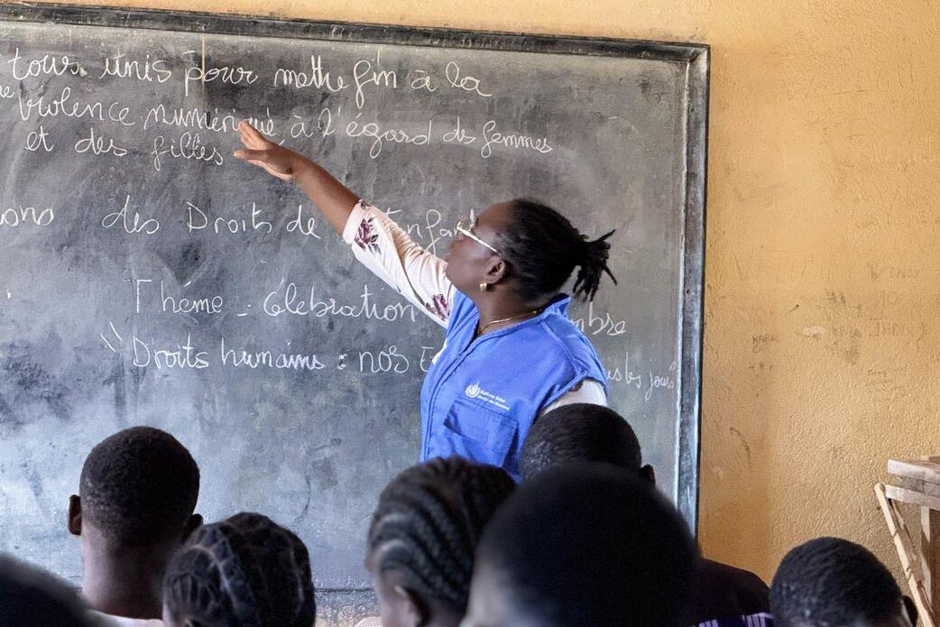 Une femme se tient devant un tableau noir, face à un groupe d'étudiants.