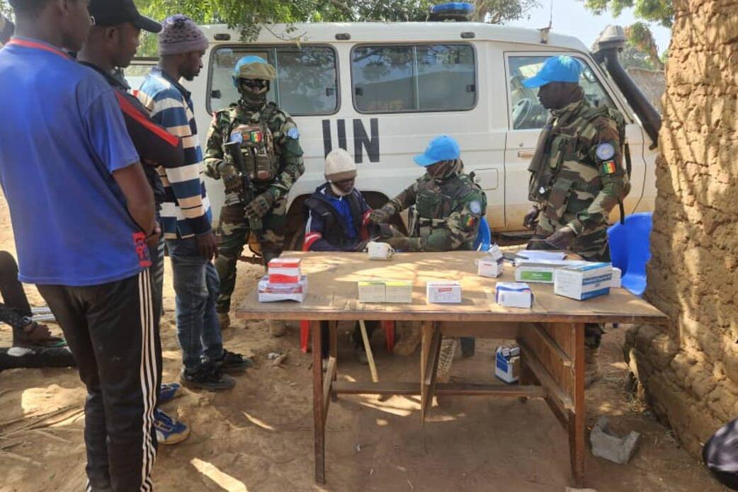 Community members and peacekeepers meet around an outdoor table, in front of a UN van