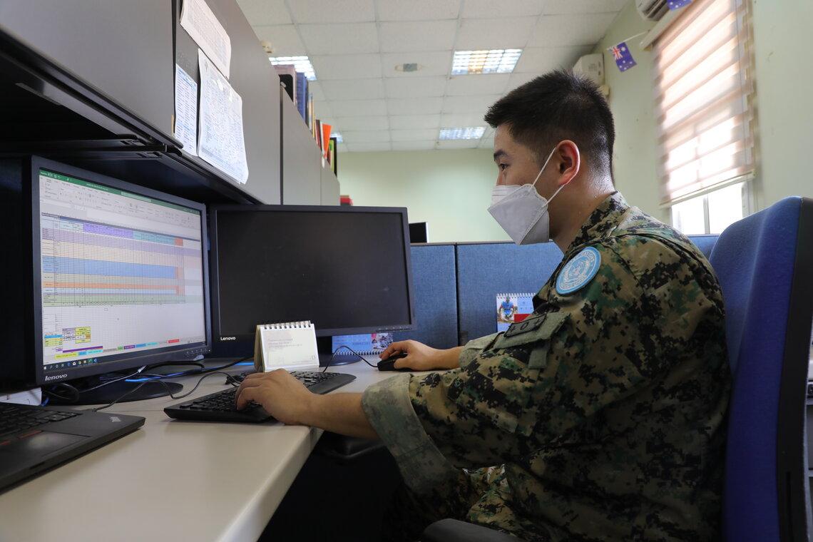 A peacekeeper sits at a desk and uses a computer.