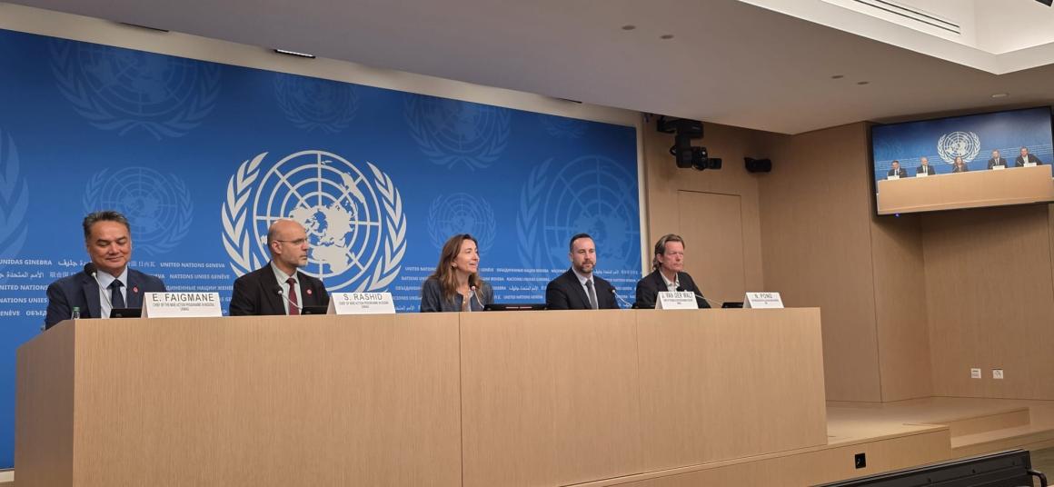 a woman is sitting in the center with four men sitting beside her in front of an UN logo background