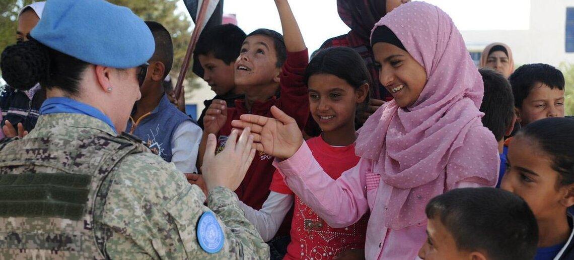 A uniformed UNDOF peacekeeper greets a group of smiling children in Syria