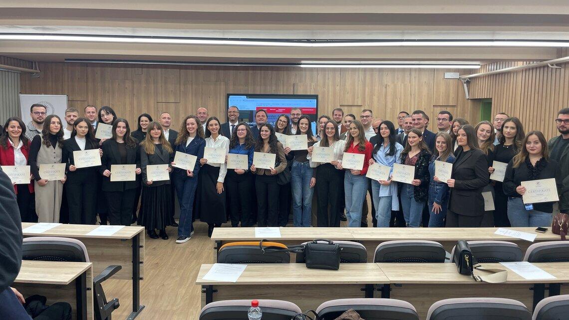 A group of graduates stand in a room holding diplomas